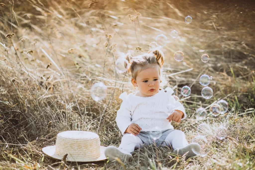little baby girl blowing soap bubbles field